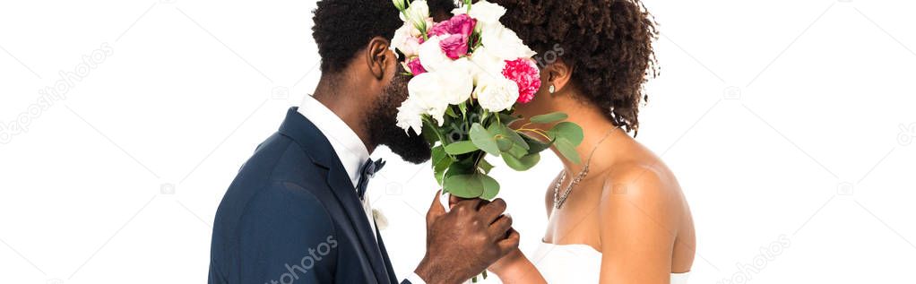 panoramic shot of african american bride and bridegroom covering faces while holding flowers isolated on white 