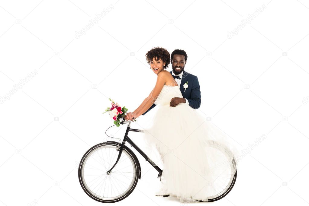 happy african american bridegroom near cheerful bride riding bicycle isolated on white 