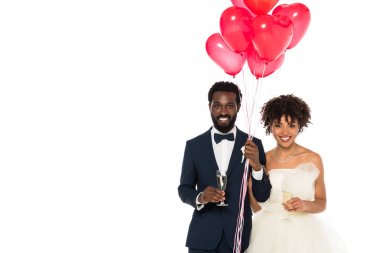 happy african american bridegroom and bride holding champagne glasses near pink balloons  isolated on white  clipart