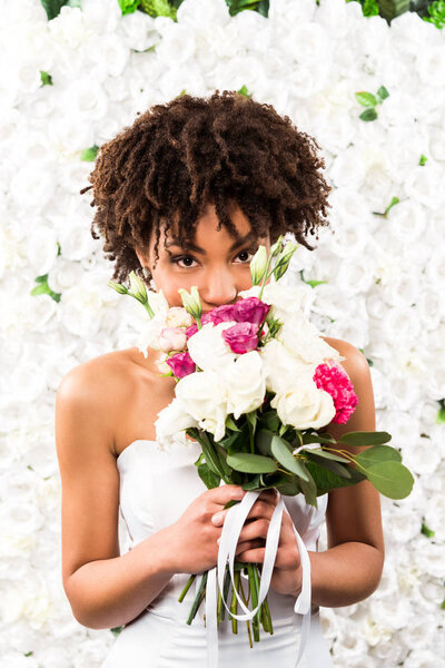 african american bride covering face while holding flowers 