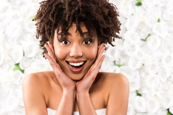 Feliz Afroamericano Novia Tocando Cara Mientras Mira Cámara Cerca Flores —  Fotos de Stock