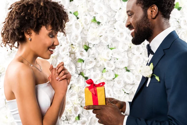 Hombre Afroamericano Feliz Dando Regalo Novia Sorprendida Cerca Flores — Foto de Stock