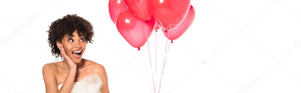 panoramic shot of excited african american bride looking at pink balloons isolated on white 