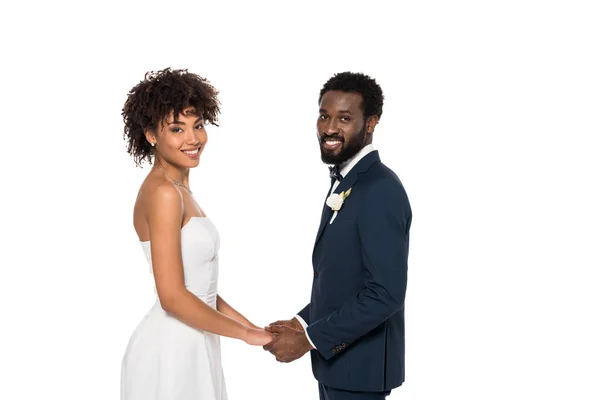 白で孤立した手を保持しながら カメラを見てウェディングドレスと花婿で幸せなアフリカ系アメリカ人の花嫁 — ストック写真