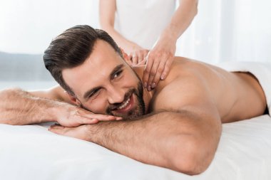 masaj masasında yatan mutlu sakallı adama masaj yapan masör seçici odak 