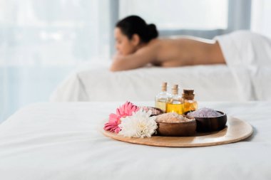 yağ şişeleri ile tepsi seçici odak, spa merkezinde esmer kadın yakın deniz tuzu ve çiçekler ile kase 