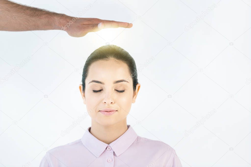 cropped view of healer putting hand above head of attractive woman with closed eyes on white 