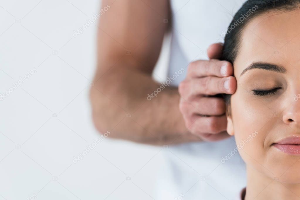 cropped view of masseur putting hands on temples of woman isolated on white 