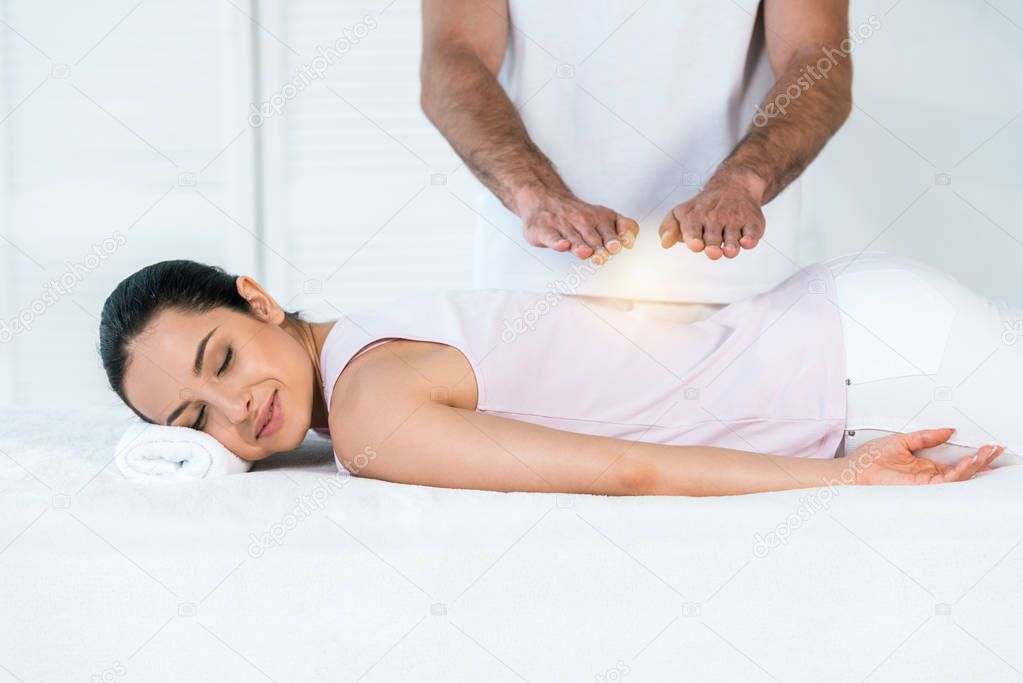 cropped view of healer putting hands above attractive woman with closed eyes lying on massage table