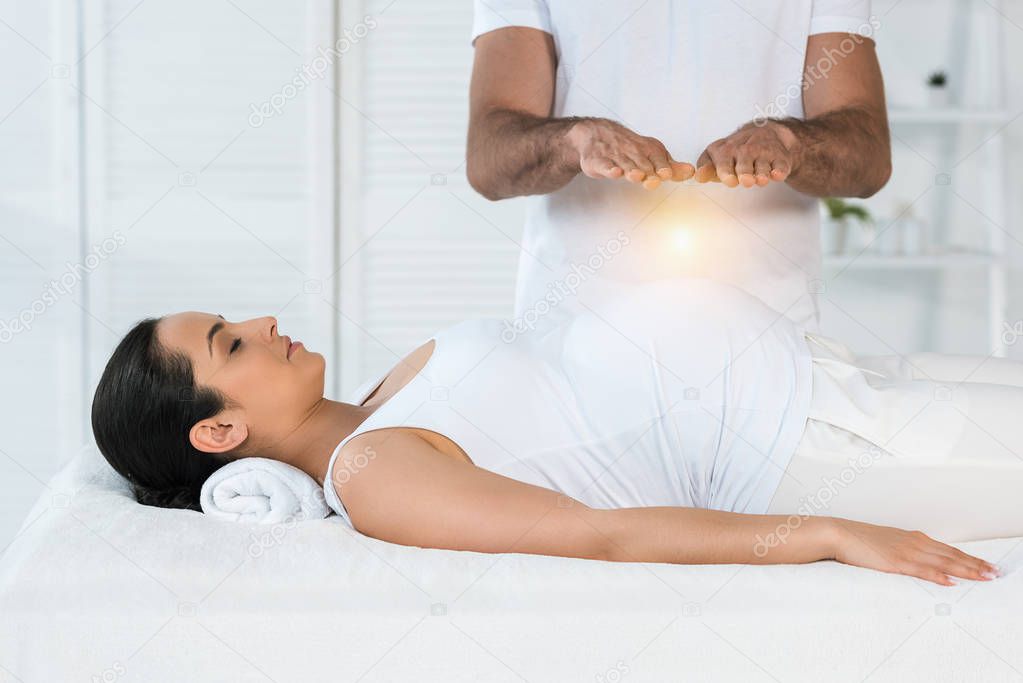 cropped view of man healing attractive pregnant woman lying on massage table 