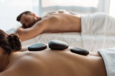 spa merkezinde erkek yakınında taş masajı olan kadının seçici odak 