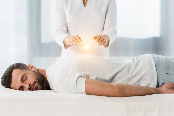 обрезанный вид женщины исцеляющей мужчину, положив руки над телом
