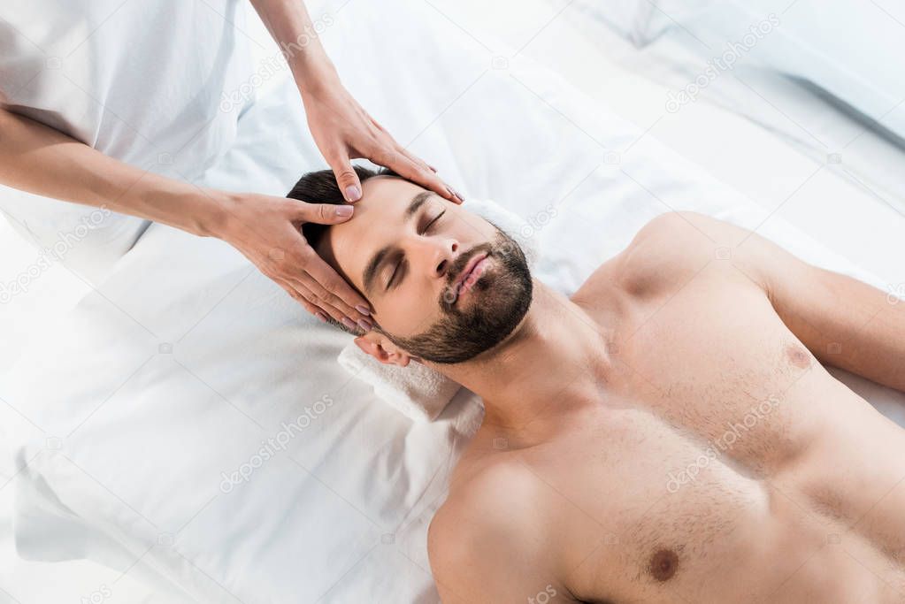 overhead view of masseur doing massage to handsome man with closed eyes