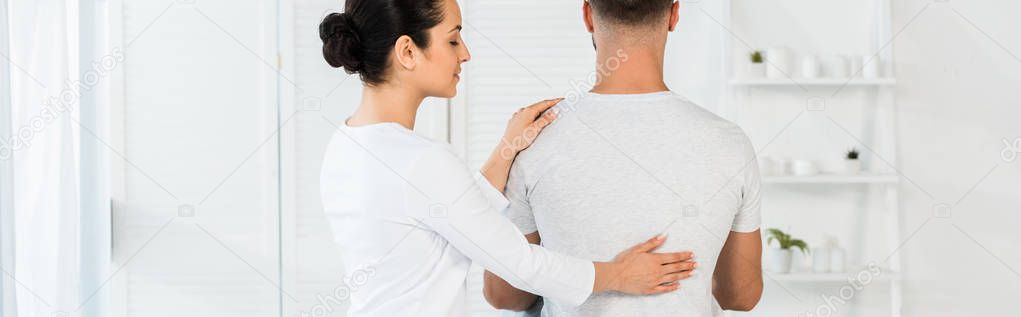 panoramic shot of man sitting on massage table near attractive healer 