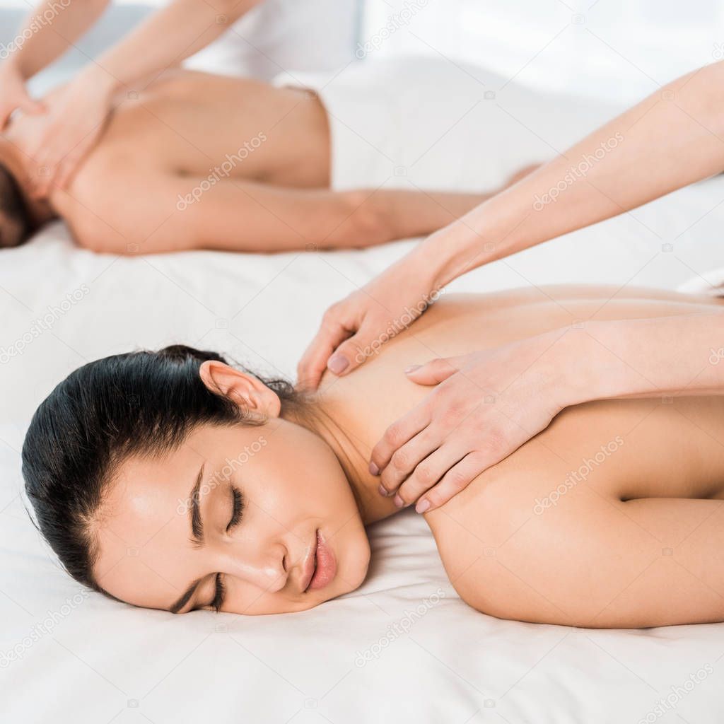 selective focus of masseur doing massage to attractive woman with closed eyes near man 