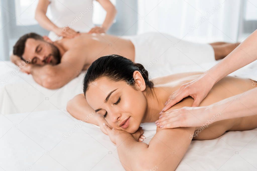 selective focus of masseur doing massage to attractive woman with closed eyes near bearded man 