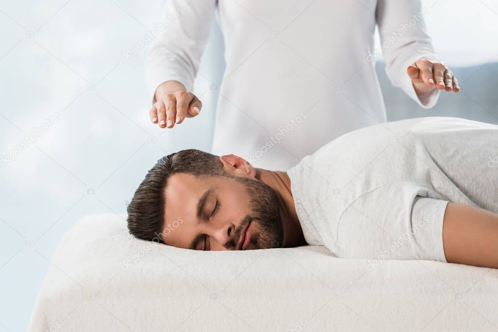 cropped view of healer with hands above body of man on massage table 