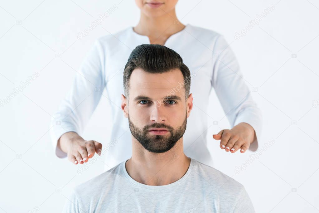 cropped view of healer holding hands near shoulders of handsome man isolated on white 