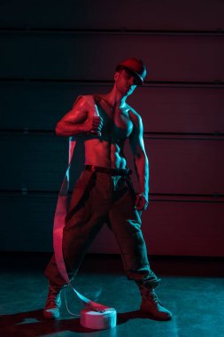 full length view of shirtless sexy fireman holding fire hose in darkness clipart