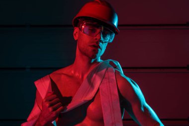 sexy shirtless fireman in protective helmet holding fire hose in darkness clipart