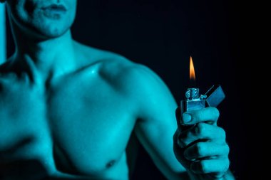 cropped view of sexy shirtless man holding lighter in darkness clipart