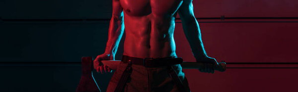panoramic shot of shirtless fireman holding flat head axe in darkness