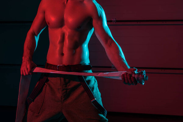 cropped view of shirtless fireman holding fire hose in darkness