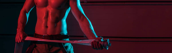 panoramic shot of sexy fireman holding fire hose in darkness