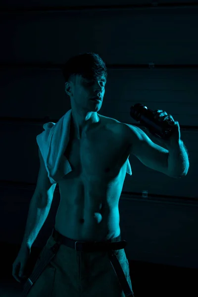 性感的无衬衫男子与毛巾抱着运动瓶在黑暗中 — 图库照片