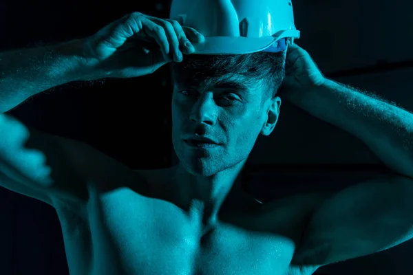性感的无衬衫消防员在黑暗中触摸防护帽 — 图库照片