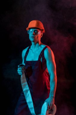 sexy fireman in hardhat and protective goggles holding fire hose in smoke on black clipart