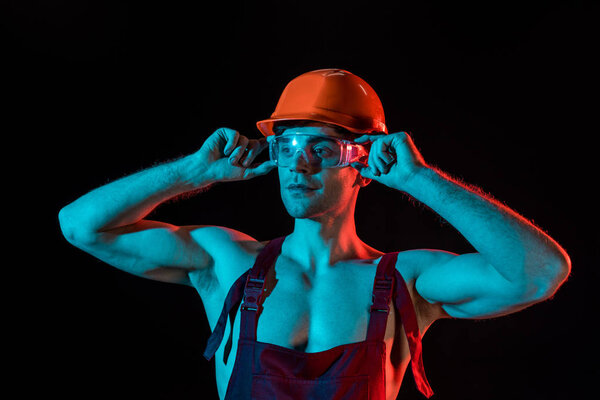 sexy fireman in overall, hardhat and protective goggles isolated on black