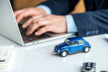 selective focus of man in formal wear using laptop at table with blue toy car clipart