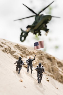 arka planda helikopter ile kum üzerinde Amerikan bayrağı tutan silah ile oyuncak askerin seçici odak