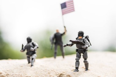 selective focus of toy soldiers with weapon and american flag on sand clipart
