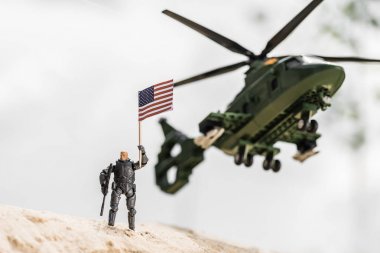 helikopter in yanında kum üzerinde dururken Amerikan bayrağı tutan oyuncak asker
