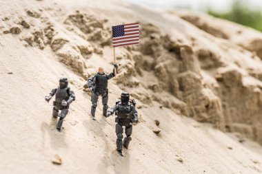 toy soldiers with weapon standing on sand and holding american flag clipart