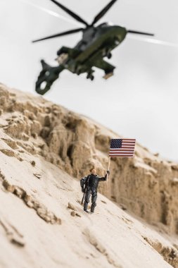 selective focus of toy soldier holding american flag on sand dune clipart