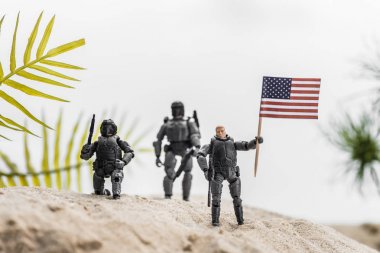 selective focus of toy soldiers holding american flag on sand hill clipart