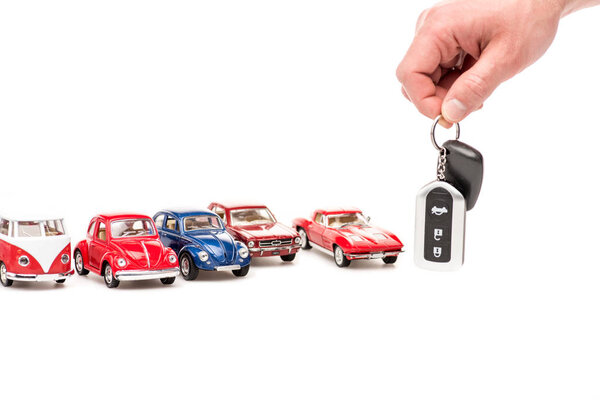 обрезанный вид человека, держащего ключи и красочные игрушечные автомобили на белом
