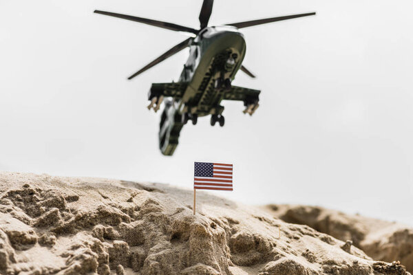 selective focus of small american flag on sand dune with military helicopter above