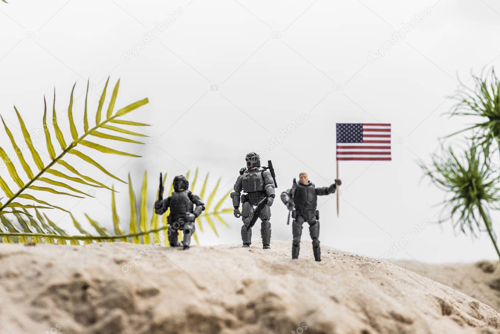 selective focus of toy soldiers holding american flag on sand dune