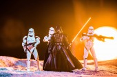 KYIV, UKRAINE - MAY 25, 2019: white imperial stormtroopers with guns and  Darth Vader with lightsaber on black background with bright sun