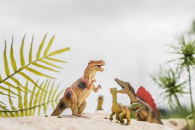 selective focus of toy dinosaurs on sand dune among tropical plants