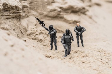 selective focus of plastic toy soldiers on sand dune with guns clipart
