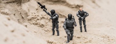 selective focus of plastic toy soldiers on sand dune with guns, panoramic shot clipart