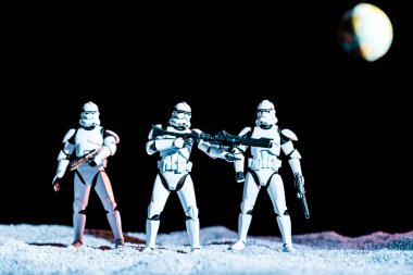 toy white imperial stormtroopers with guns on black background with planet Earth
