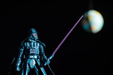 selective focus of Darth Vader figurine with lightsaber on black background with planet Earth