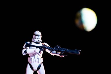 white imperial stormtrooper figure with gun on black background with blurred planet Earth
