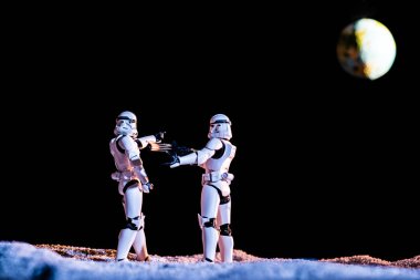 white imperial stormtrooper aiming with toy gun at another on black background with planet Earth